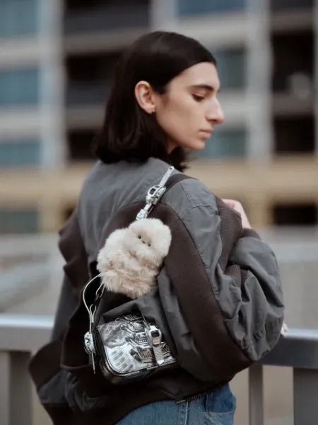 Pink plush companion perched on the strap of a silver bag