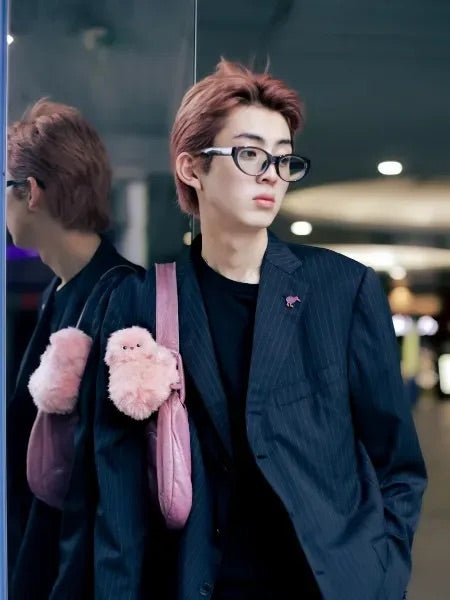 Person in a pinstripe blazer with a pink plush companion on a pink bag strap