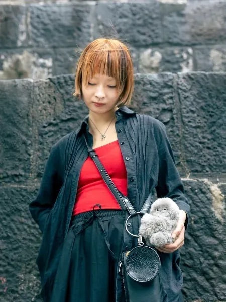 Woman in a camo jacket holding a gray plush companion on a black ring-handle bag