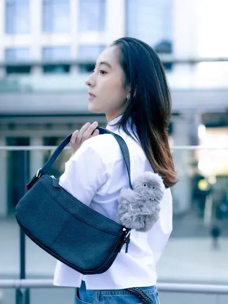 Woman in a white shirt with a gray plush companion on her shoulder bag strap